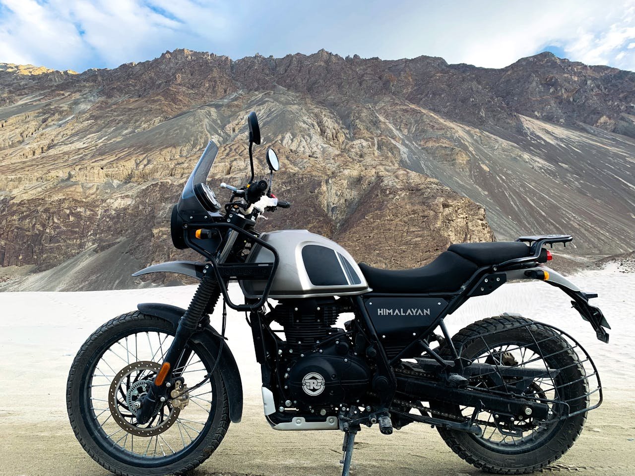 gallery-1 A rugged Royal Enfield Himalayan motorbike parked against the scenic mountains of Jammu.