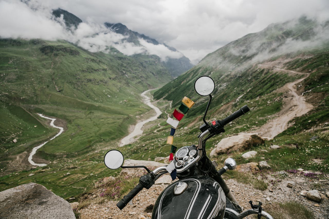 services-03 Motorcycle parked in a stunning green valley with winding roads and cloudy mountains.